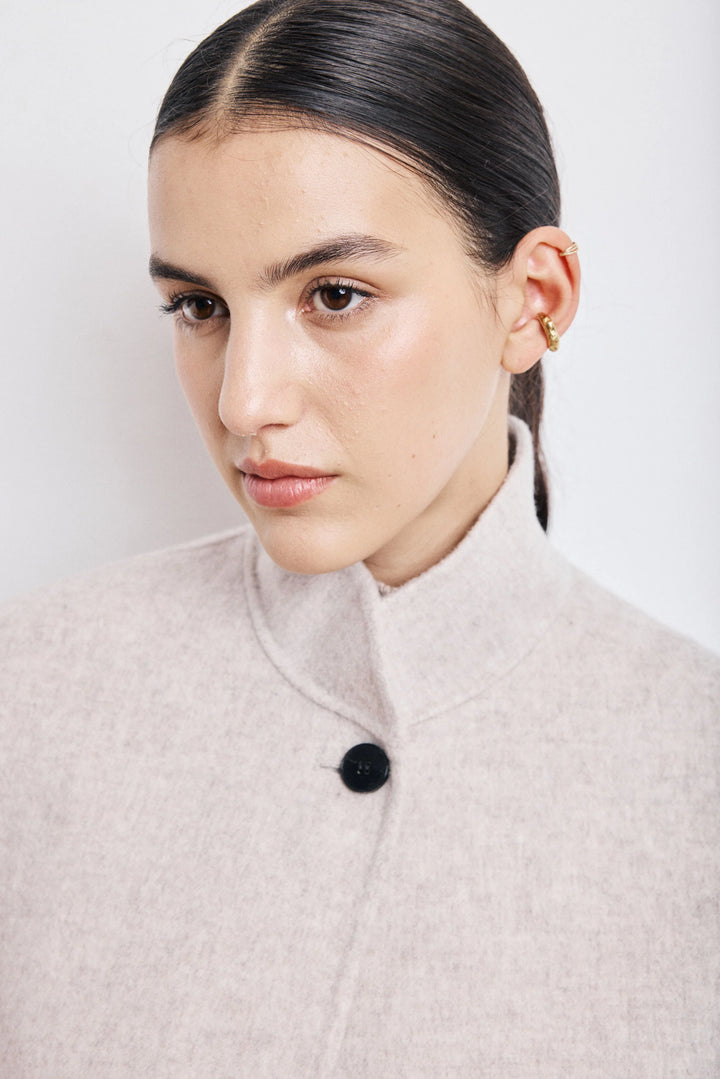 Woman wearing a light gray coat with a black button against a white background