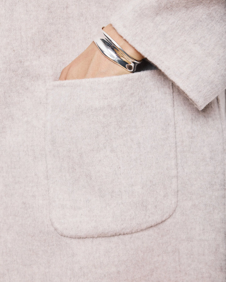 Close-up of a light gray coat with a pocket containing a phone and wallet.