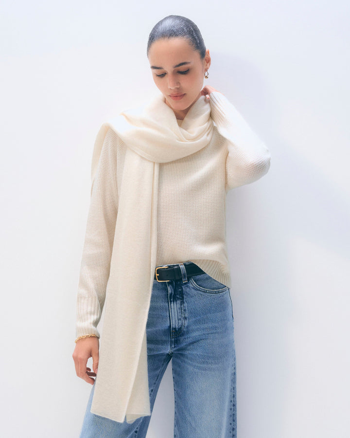 Person wearing a cream scarf and blue jeans against a white background