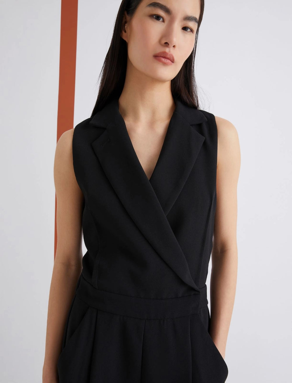 Woman wearing a black sleeveless dress against a plain background