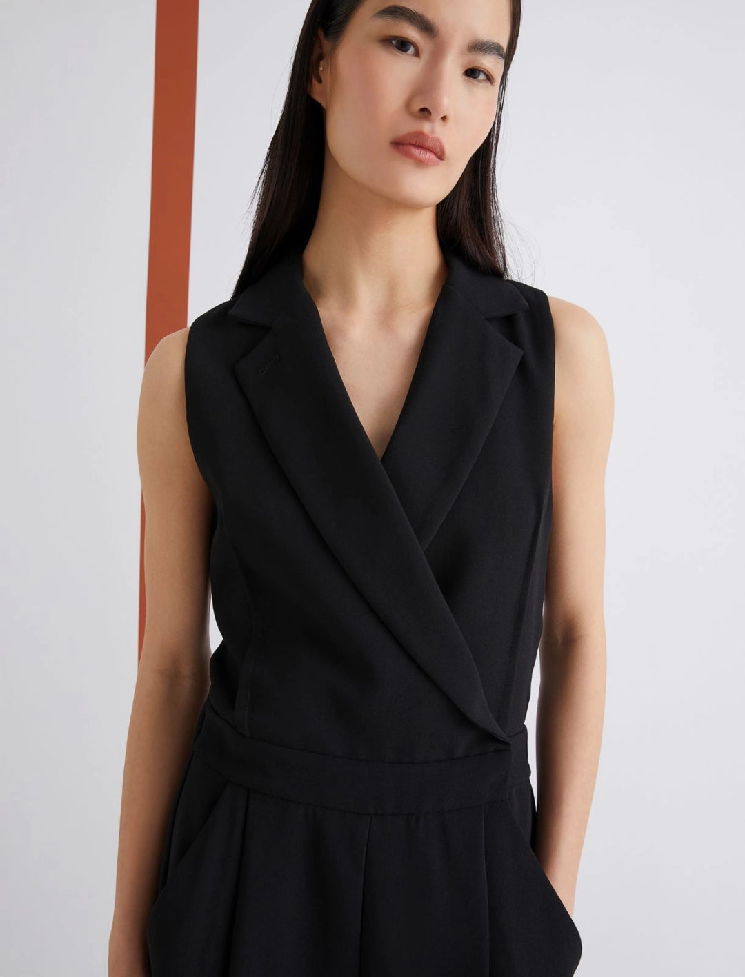 Woman wearing a black sleeveless dress against a plain background