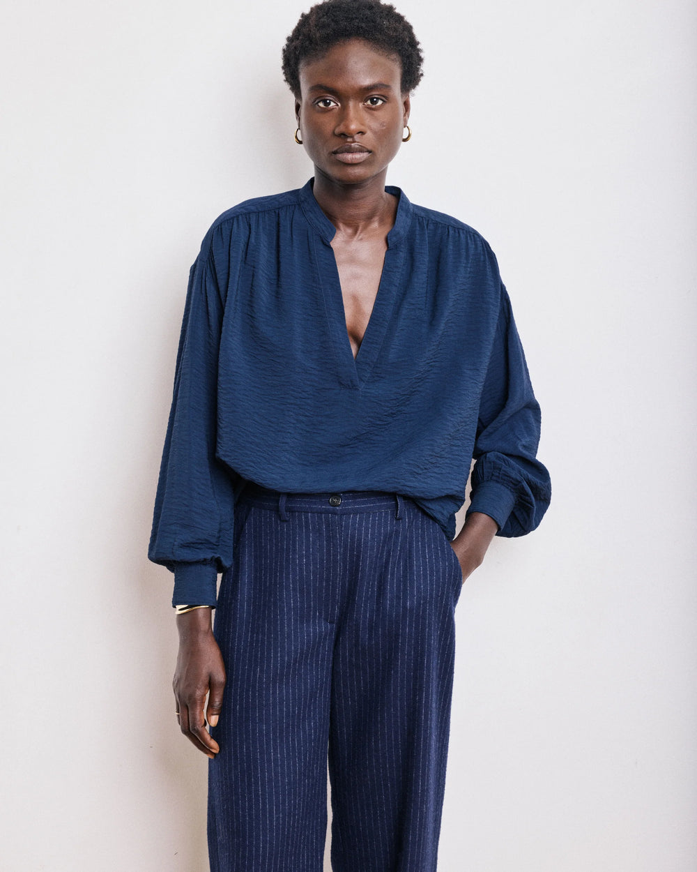 Person wearing a blue blouse and dark pants against a white background