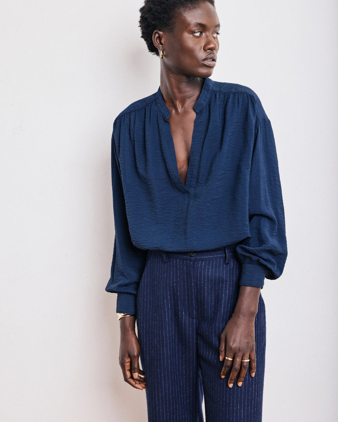 Person wearing a blue blouse and dark pants against a light background