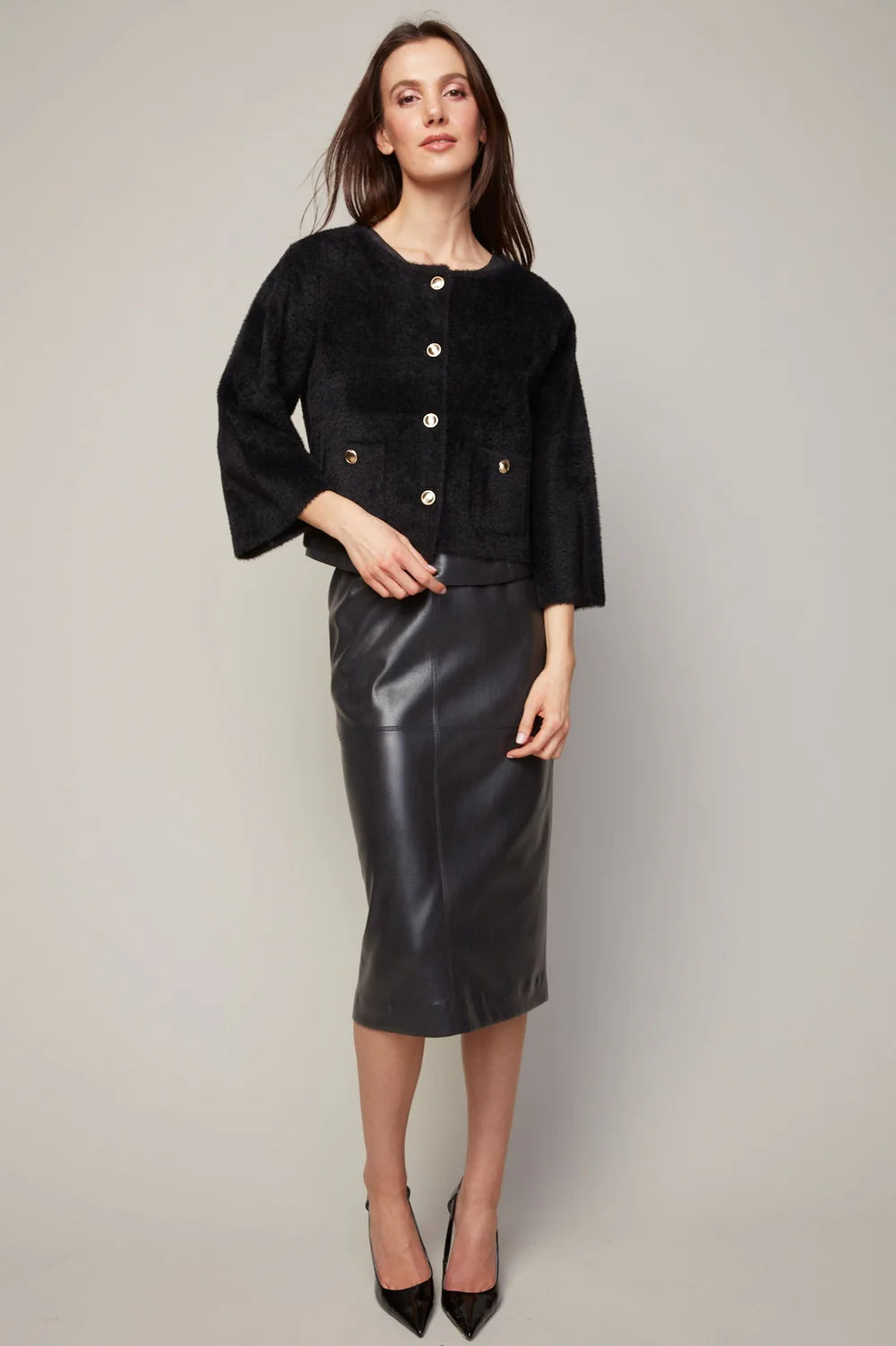 Woman wearing a black textured jacket and leather skirt on a plain background