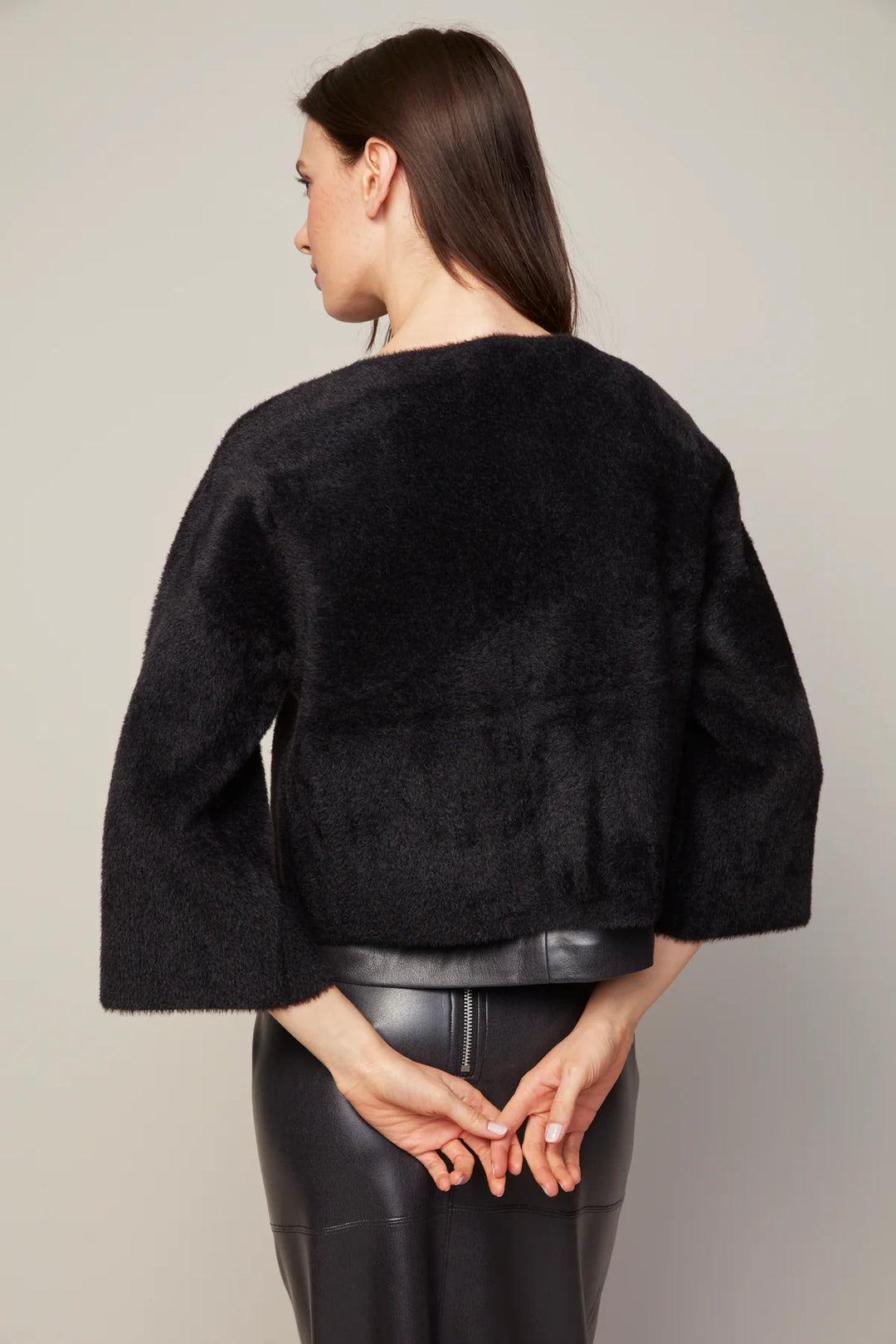 Woman wearing a black textured jacket and black pants against a plain background