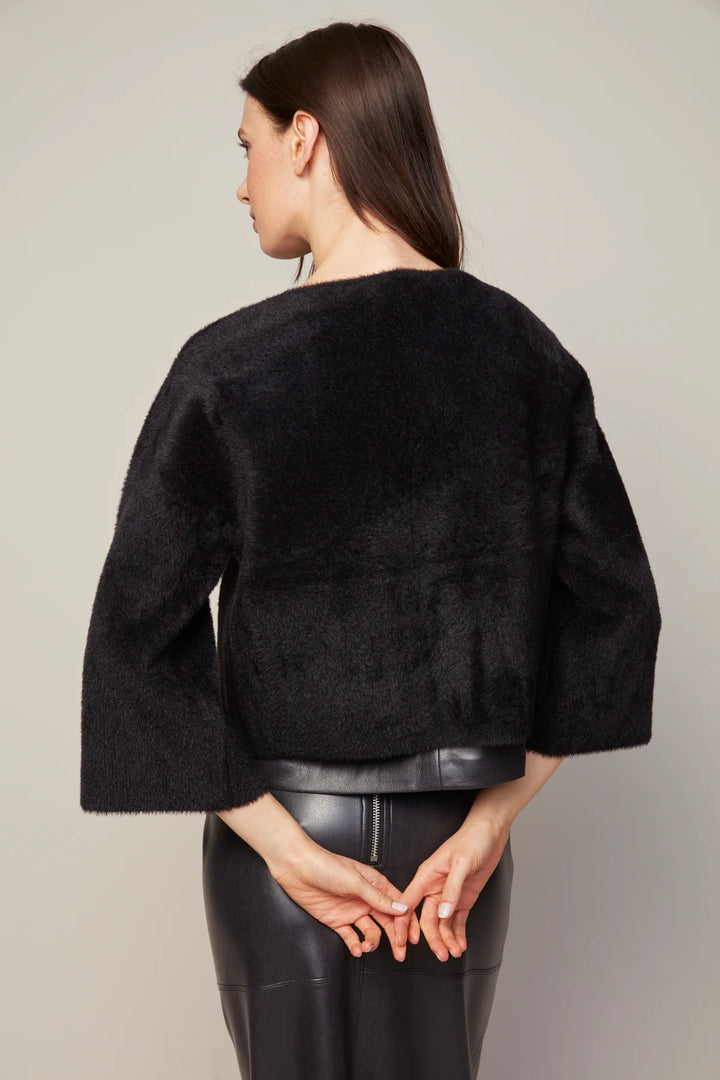 Woman wearing a black textured jacket and black pants against a plain background