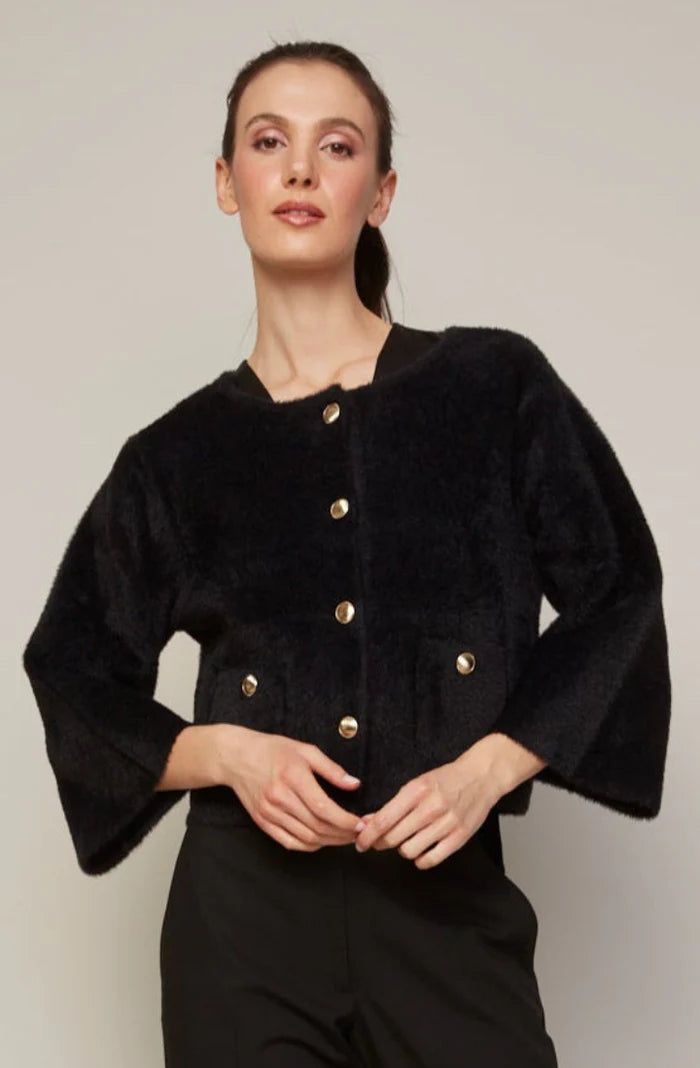 Woman wearing a black textured jacket with gold buttons against a plain background