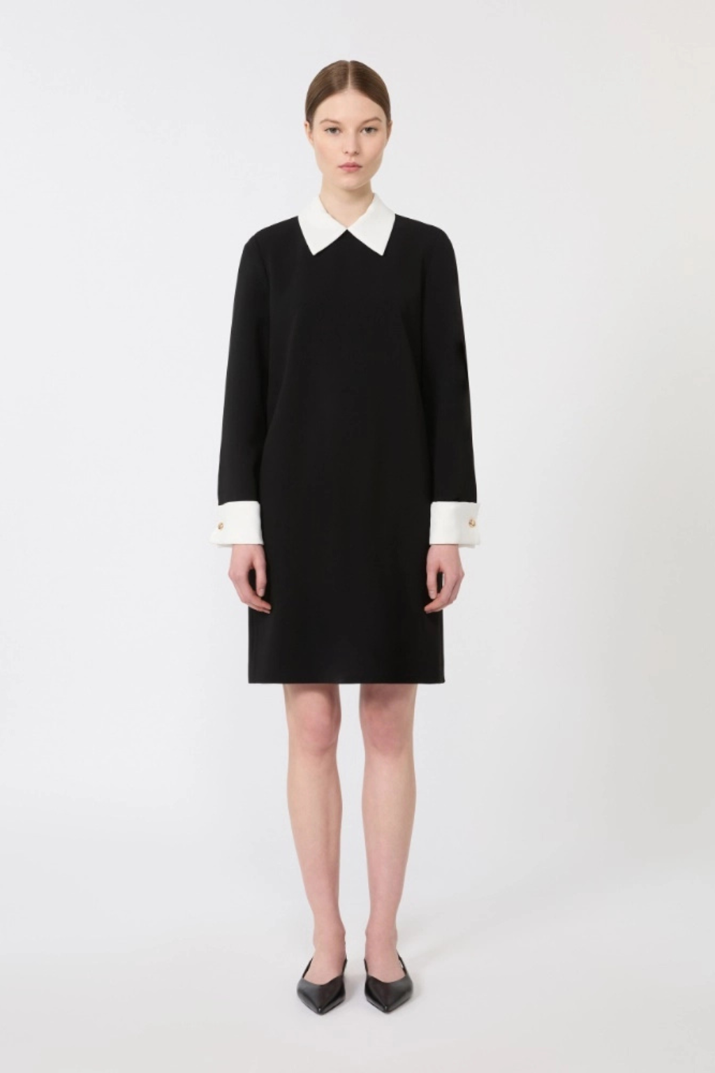 Black dress with white collar and cuffs worn by a model on a white background