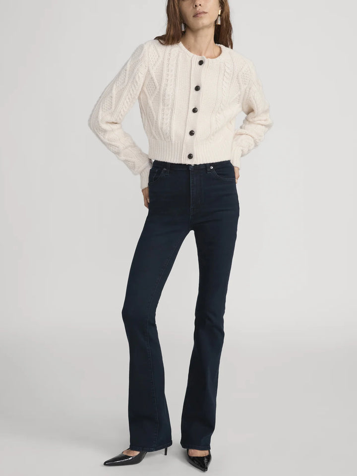 Woman wearing a cream sweater and dark blue jeans on a white background